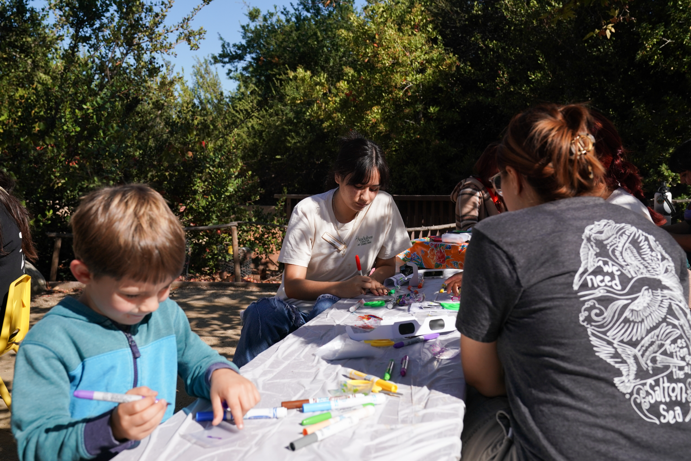 A diverse group of people of varying ages make art outside at the Audubon Center at Debs Park.